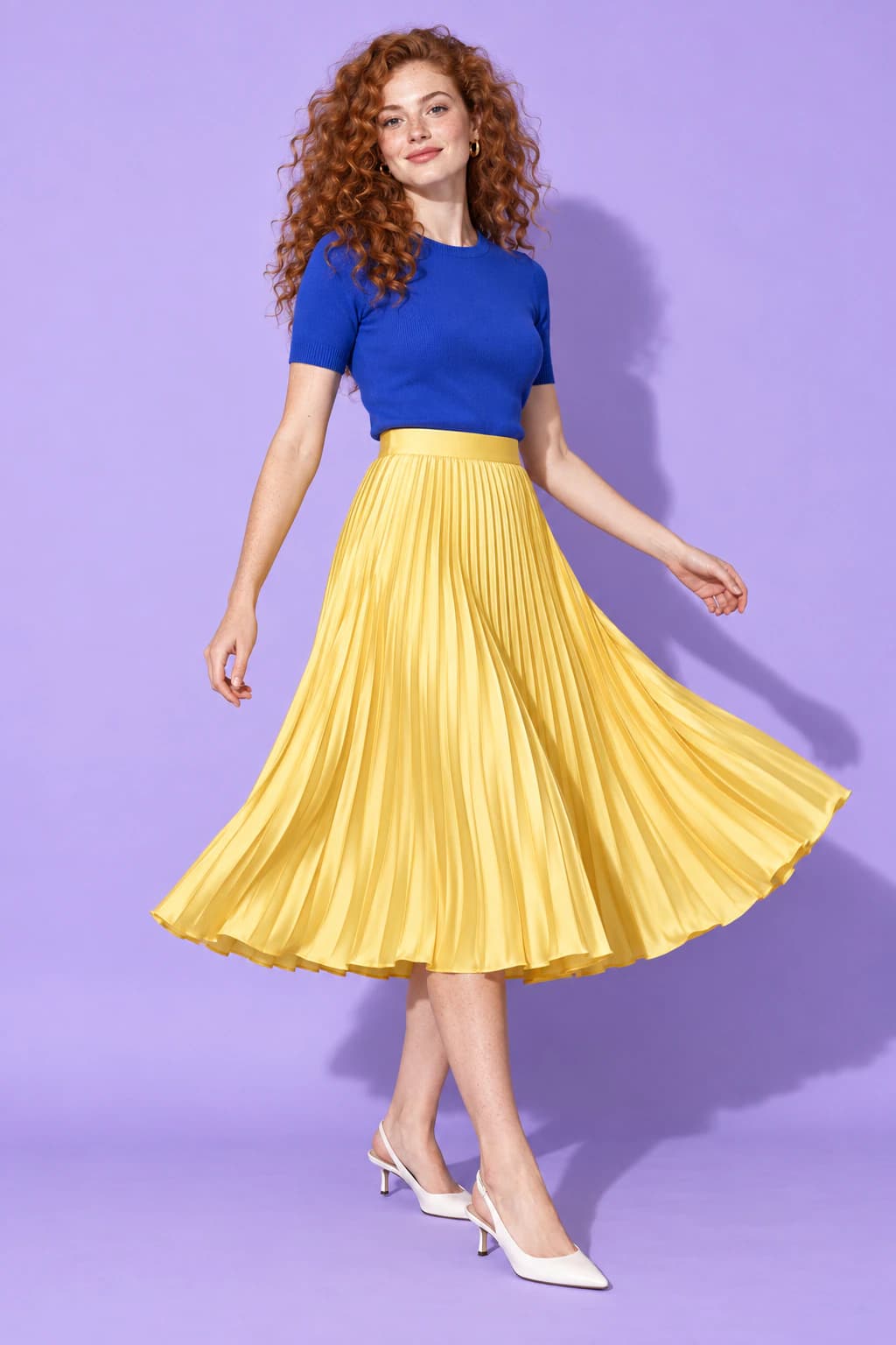 Model twirling in a lemon-yellow pleated satin midi skirt and cobalt knit top on a lilac backdrop