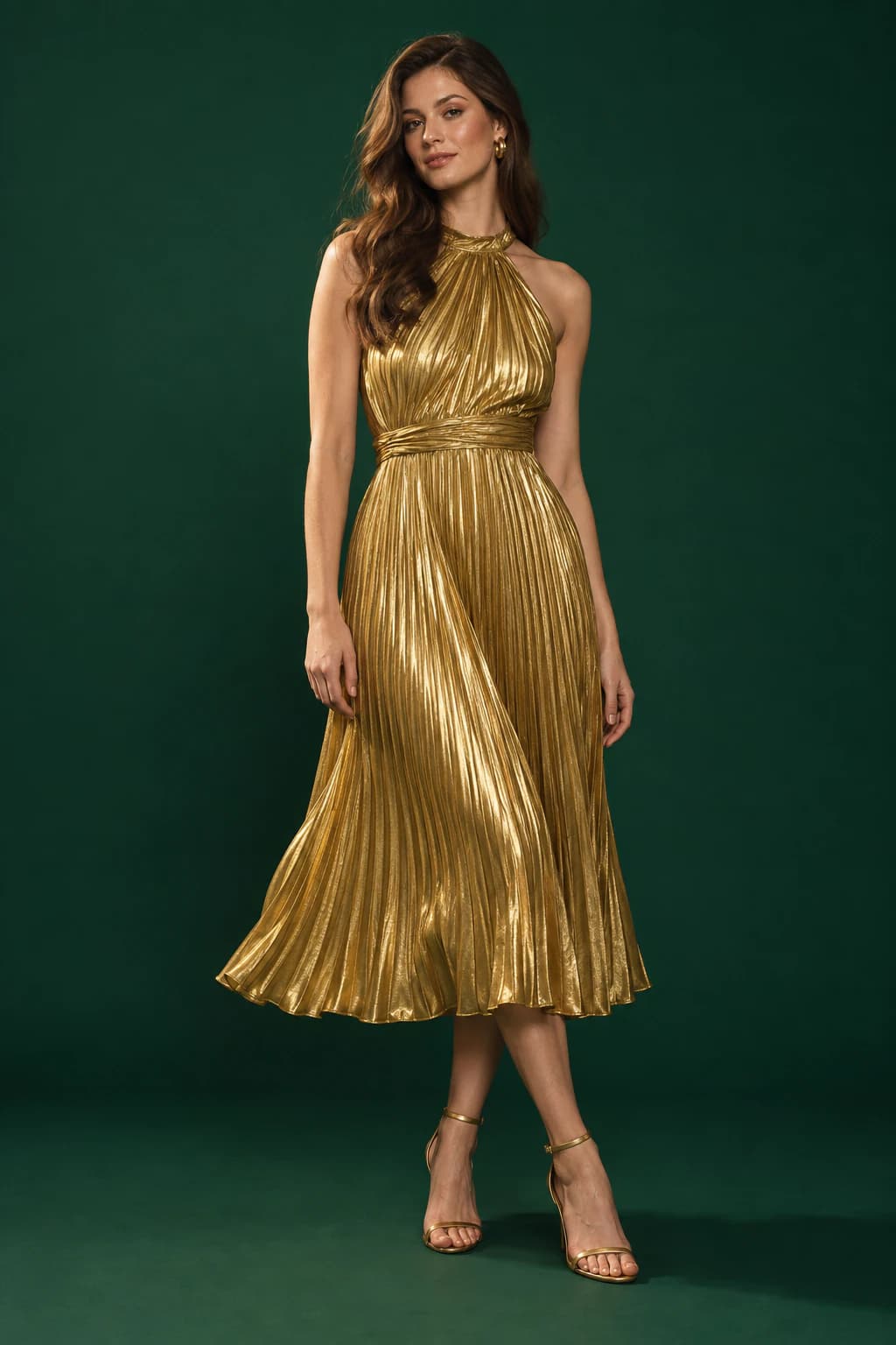 Model in a pleated gold lame halter midi dress on a deep bottle-green backdrop