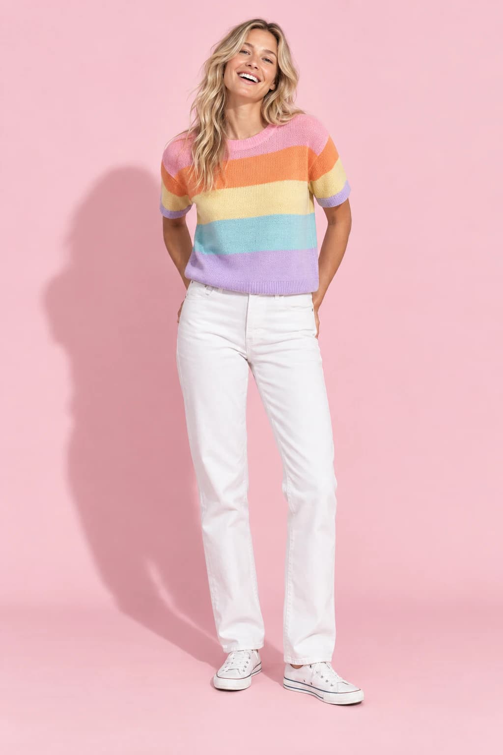 Model in a multicolour sorbet-striped knit tee and white jeans on a blush-pink backdrop